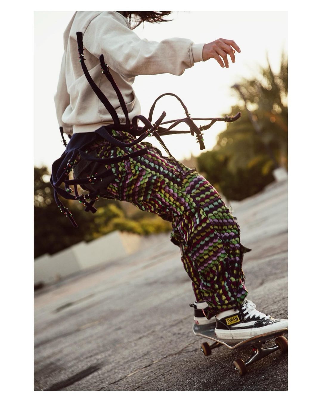 Person skateboarding outdoors wearing patterned pants and a harness-like garment. The subject is captured in motion at a low angle.