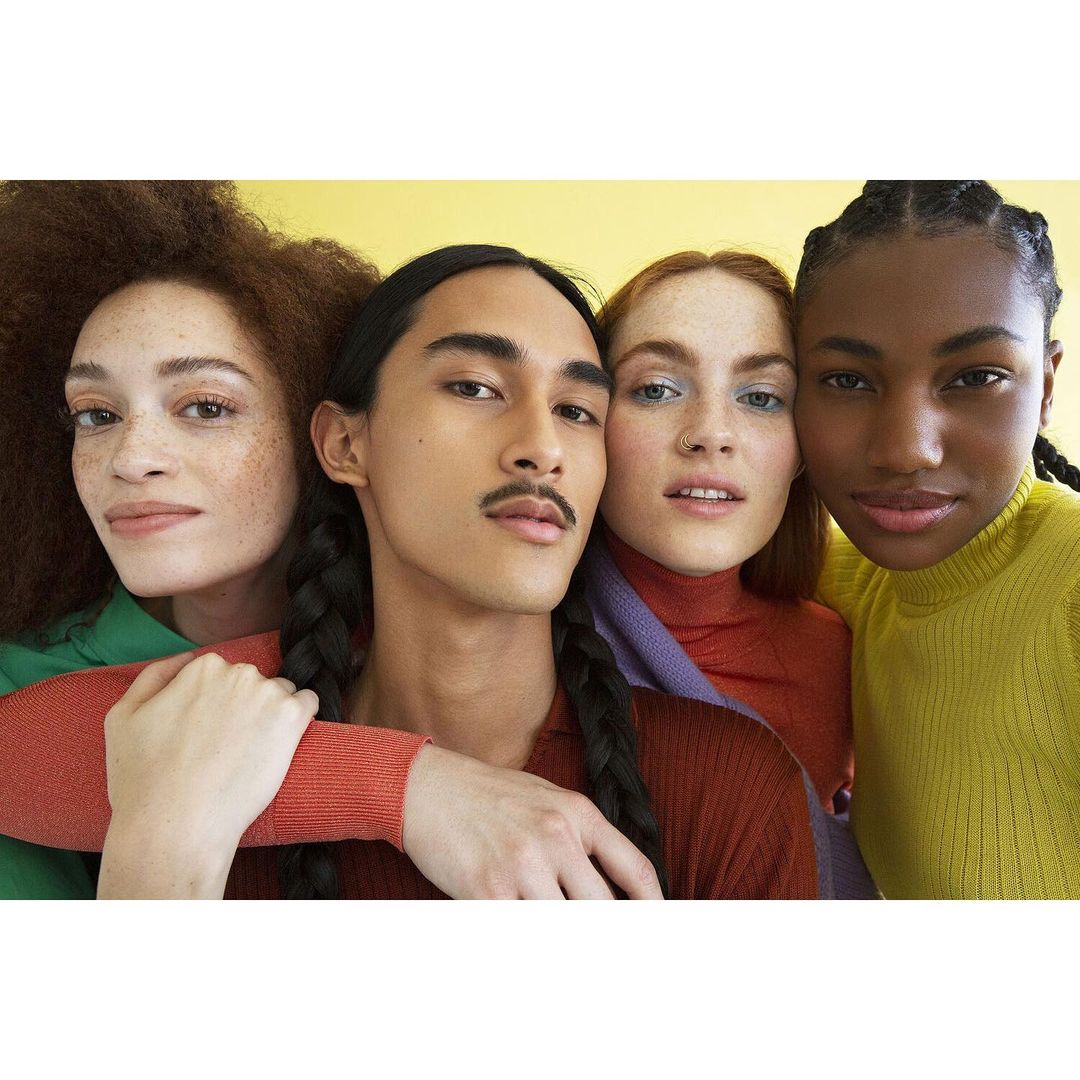 A group of four models posing in a close studio shot, showcasing diversity in skin tones, hair types, and modern fashion aesthetic.
