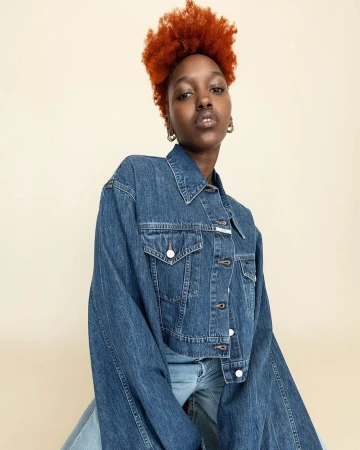 Portrait of a black woman with vibrant red hair wearing a blue denim jacket against a neutral backdrop