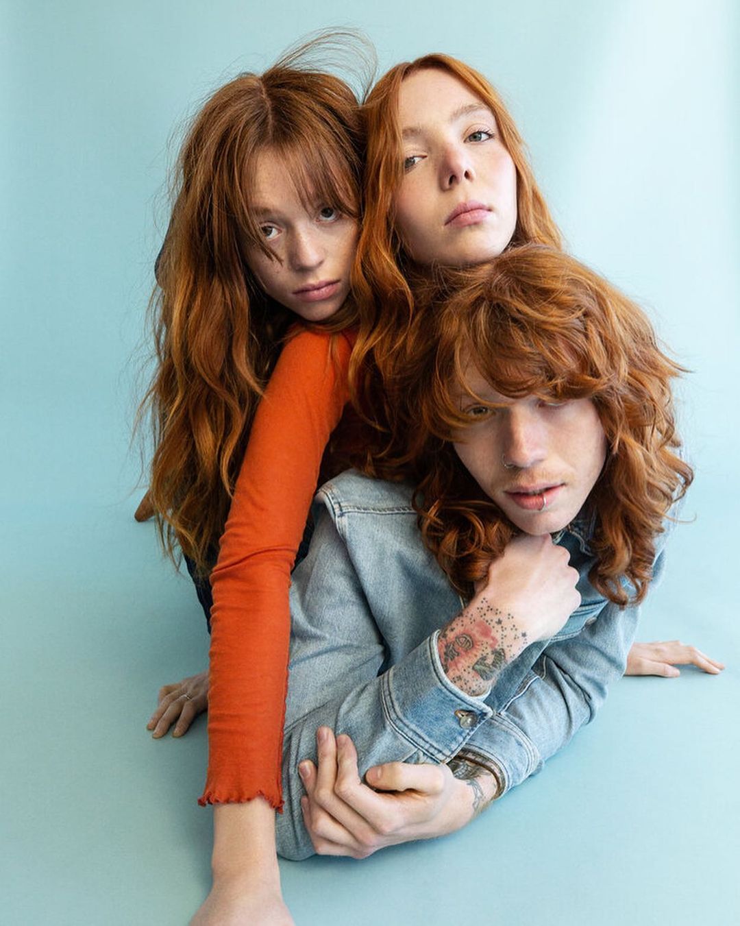 Three red-haired people clustered in a close-up studio shot. The group consists of one man and two women, their faces expressing neutral expressions.
