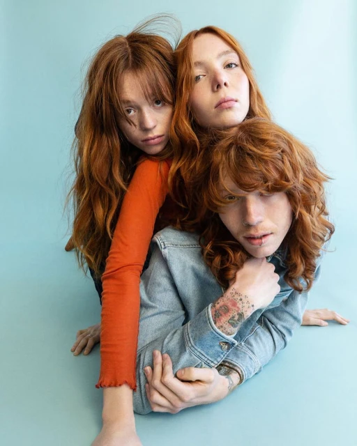 Three red-haired people clustered in a close-up studio shot. The group consists of one man and two women, their faces expressing neutral expressions.