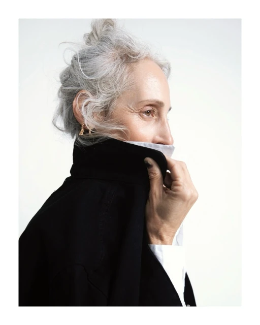 Older woman with grey hair in a studio portrait wearing a black jacket with white collared shirt. Focus on her face and elegant features.