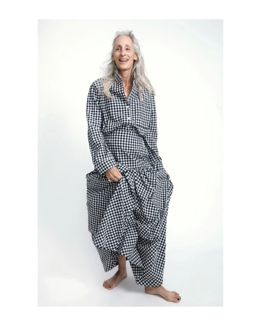 Older adult woman in a gingham patterned outfit smiles in a full shot on a white background in a fashion photography style.