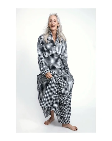 Older adult woman in a gingham patterned outfit smiles in a full shot on a white background in a fashion photography style.