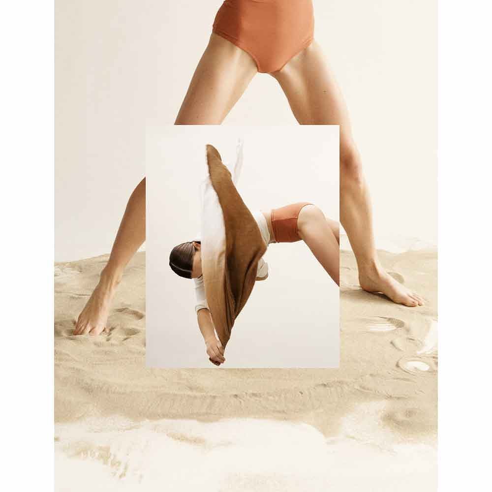 Conceptual fashion photography featuring a woman in a swimsuit bending over backward, distorted by a mirror on a sandy surface with soft lighting.
