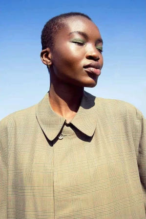 Close-up portrait of a Black woman with short hair wearing a plaid collared shirt against a clear blue sky background
