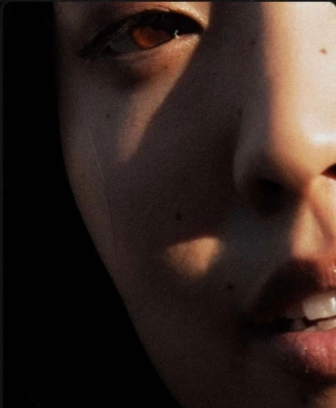 Close-up portrait of a person's face illuminated by harsh directional sunlight with visible film grain