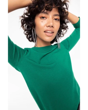 Close-up portrait of a woman with dark curly hair wearing a vibrant green top and sparkling chandelier earrings against white.