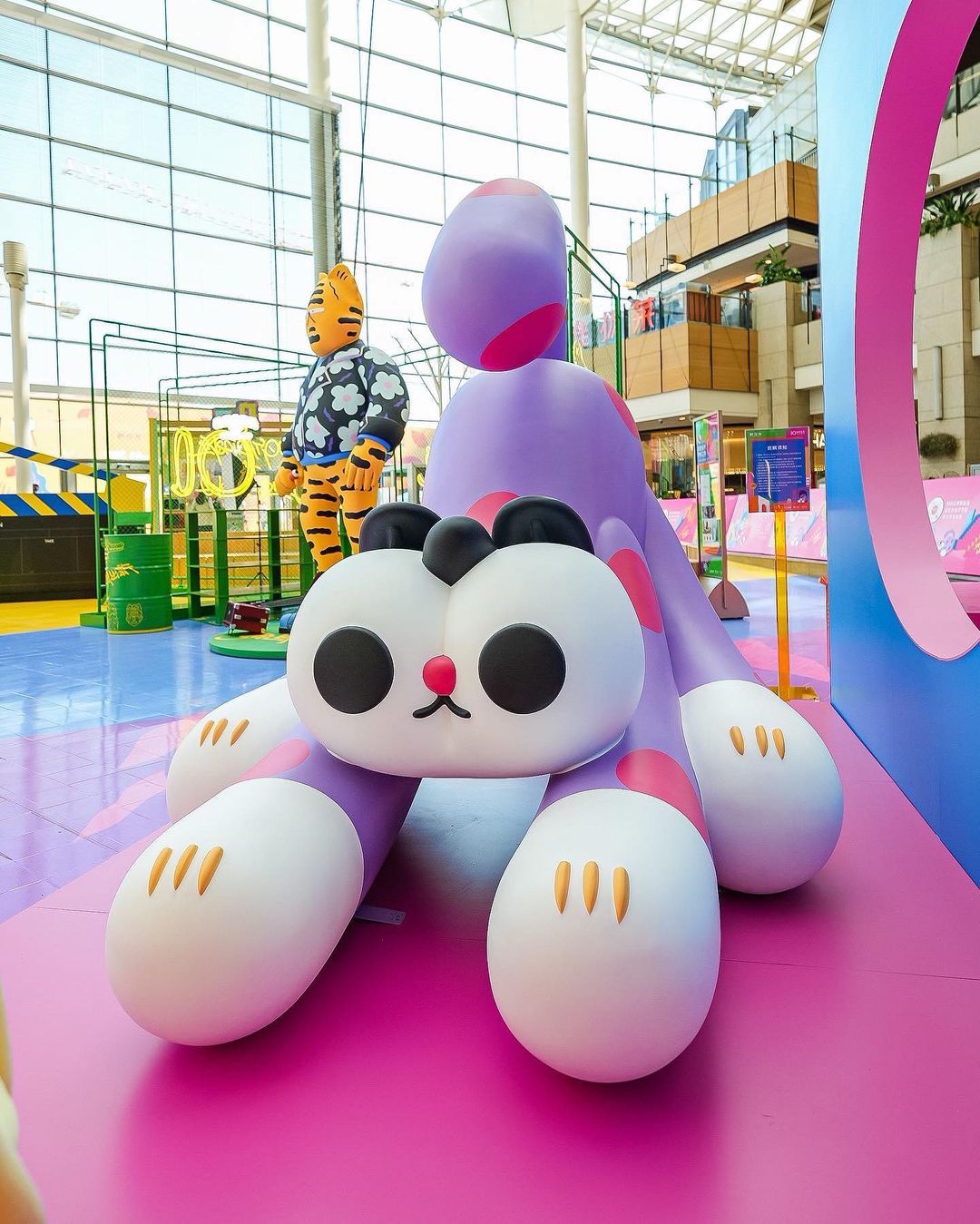 Indoor shot of a cute purple cartoon dinosaur and tiger statue against the backdrop of a mall interior, creating a whimsical scene.