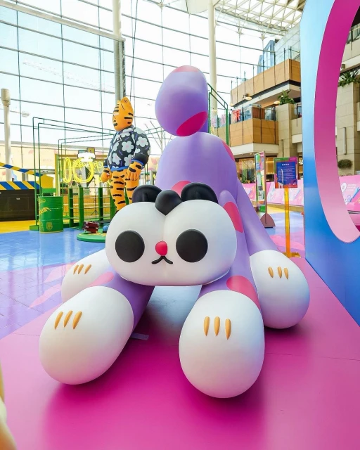 Indoor shot of a cute purple cartoon dinosaur and tiger statue against the backdrop of a mall interior, creating a whimsical scene.