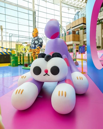 Indoor shot of a cute purple cartoon dinosaur and tiger statue against the backdrop of a mall interior, creating a whimsical scene.