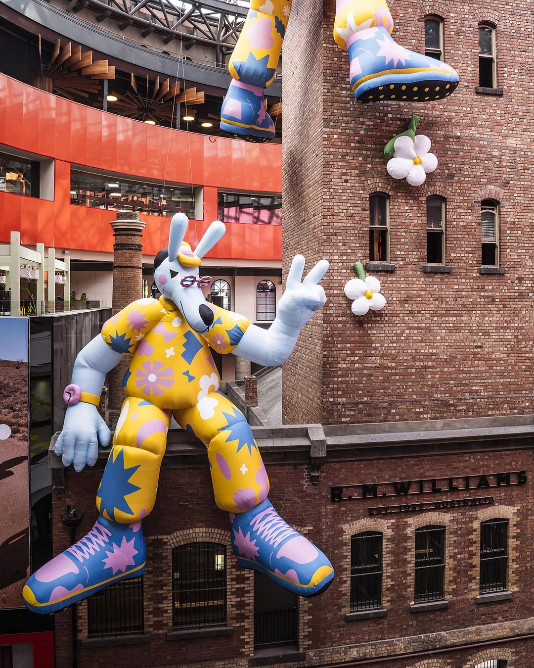 An inflatable cartoon wolf character perched on a ledge, wearing a yellow floral shirt and patterned pants, in a retail setting.