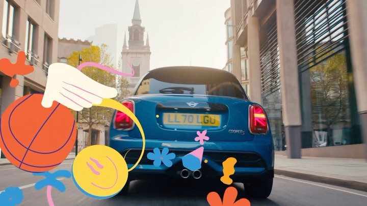 Blue Mini Cooper cruises down city street, adorned with playful cartoon graphics, creating a whimsical and lively automotive scene.