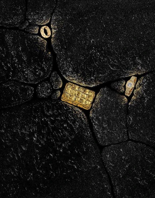 Overhead shot showcasing a ring, a woven brick, and a watch on a dark, textured surface, evoking a geological or extraterrestrial setting.