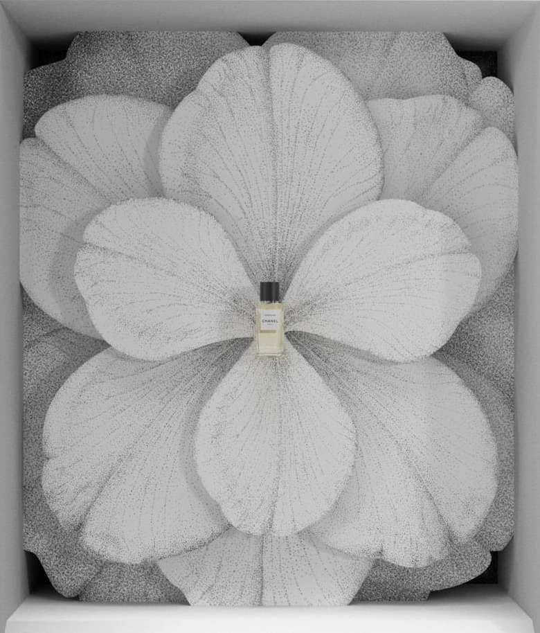 Close-up of a small perfume bottle centered against a large flower backdrop inside a white display case, product-focused composition.