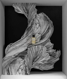 A small perfume bottle resting on an intricate, three-dimensional black and white paper sculpture with sweeping petal-like folds.