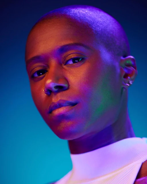 Close-up portrait of a Black adult woman with short hair in a white top, illuminated by colorful neon lighting against a blue background.