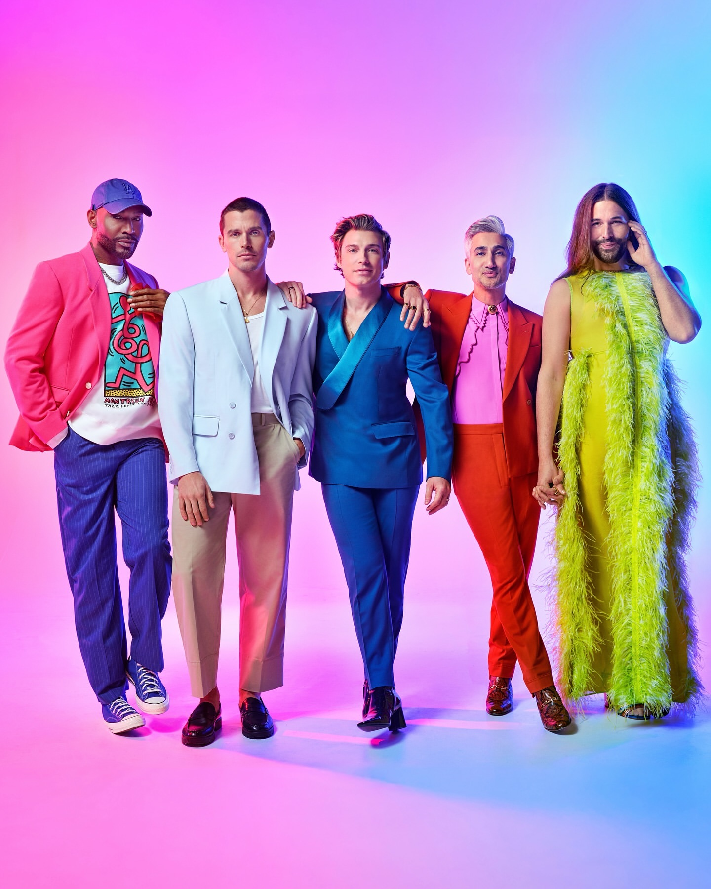 Group shot of five stylishly dressed adult males posing in front of a vibrant pink and blue gradient background in a studio setting.