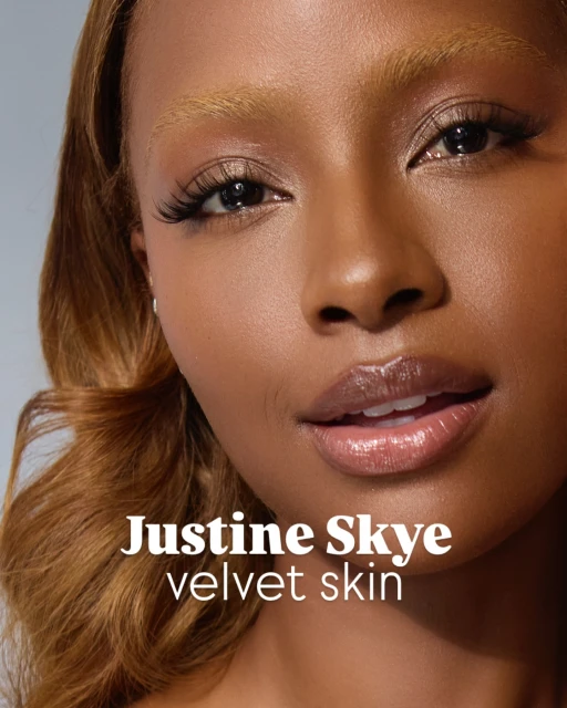 Close-up portrait of a brown-skinned woman with honey-blonde hair and glossy lips, in soft studio lighting.