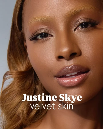Close-up portrait of a brown-skinned woman with honey-blonde hair and glossy lips, in soft studio lighting.