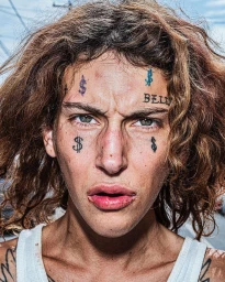 Close-up portrait of a young person with facial tattoos, curly brown hair, and a white tank top shot by Bruce Gilden.