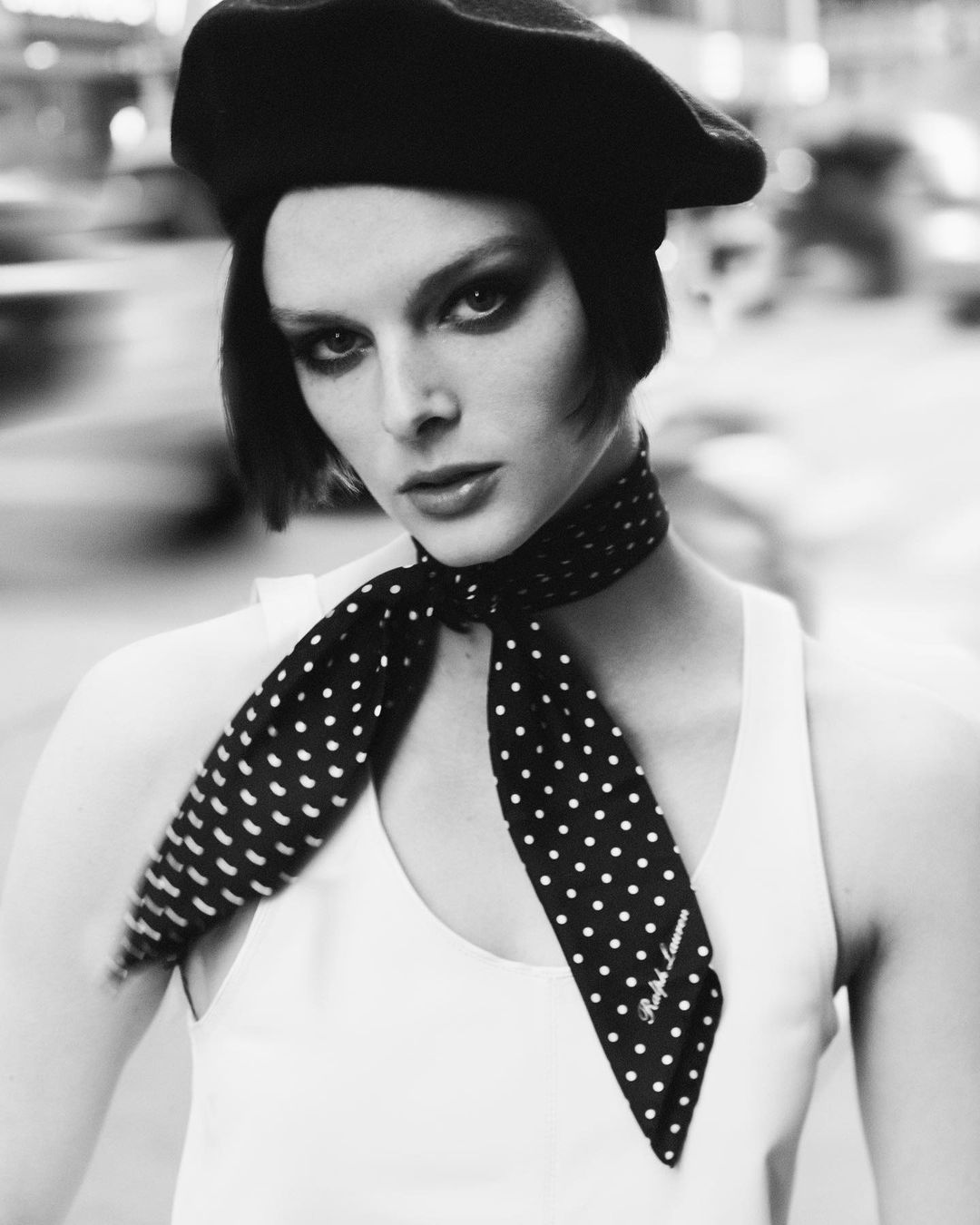Black and white portrait of an adult female wearing a black beret and a polka dot scarf. She has dark eye makeup and a neutral expression.