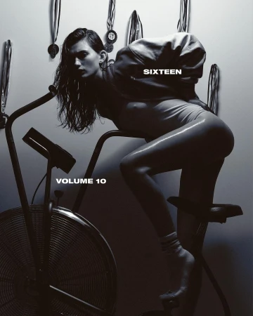 Monochrome image featuring a woman in a bodysuit leaning on an exercise bike with medals hanging in the background. Studio lighting.