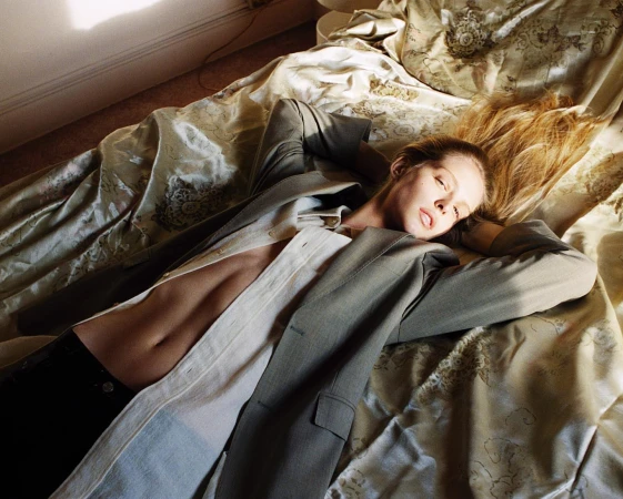 Model lying on a patterned silk bedspread wearing an open blazer and unbuttoned shirt shot by Bryan Liston.