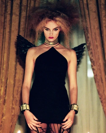 Model with voluminous hair and black angel wings wearing a halter minidress and metallic cuffs by Bryan Liston