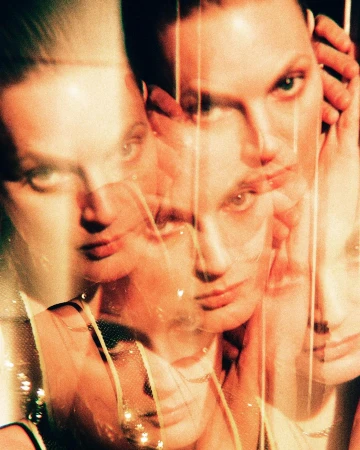 Close-up portrait of two fair-skinned adult models with neutral expressions, layered with transparent effects and a blurred focus.
