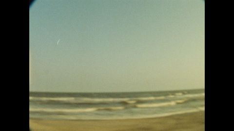 Beach landscape featuring gentle ocean waves meeting tan sand under a clear blue sky, captured with a vintage aesthetic and vignette.
