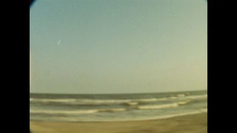 Beach landscape featuring gentle ocean waves meeting tan sand under a clear blue sky, captured with a vintage aesthetic and vignette.