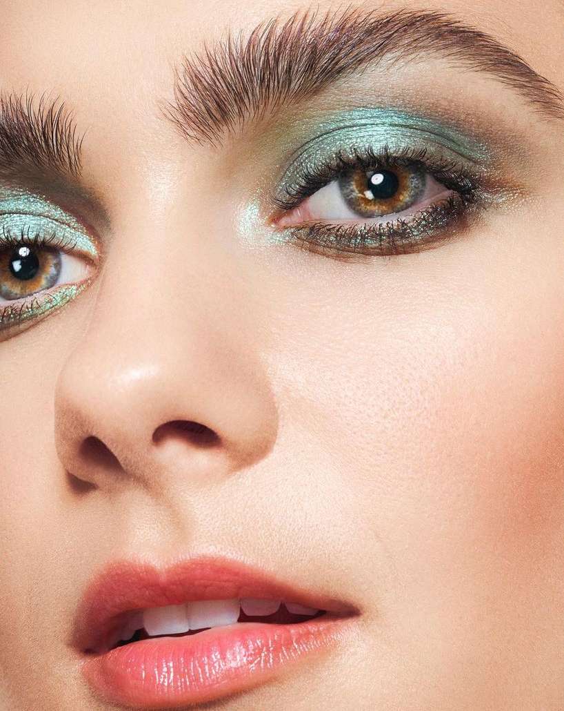 Close-up of a woman's face showcasing vibrant turquoise eyeshadow, well-defined eyebrows, and glossy lips in a beauty-focused composition.