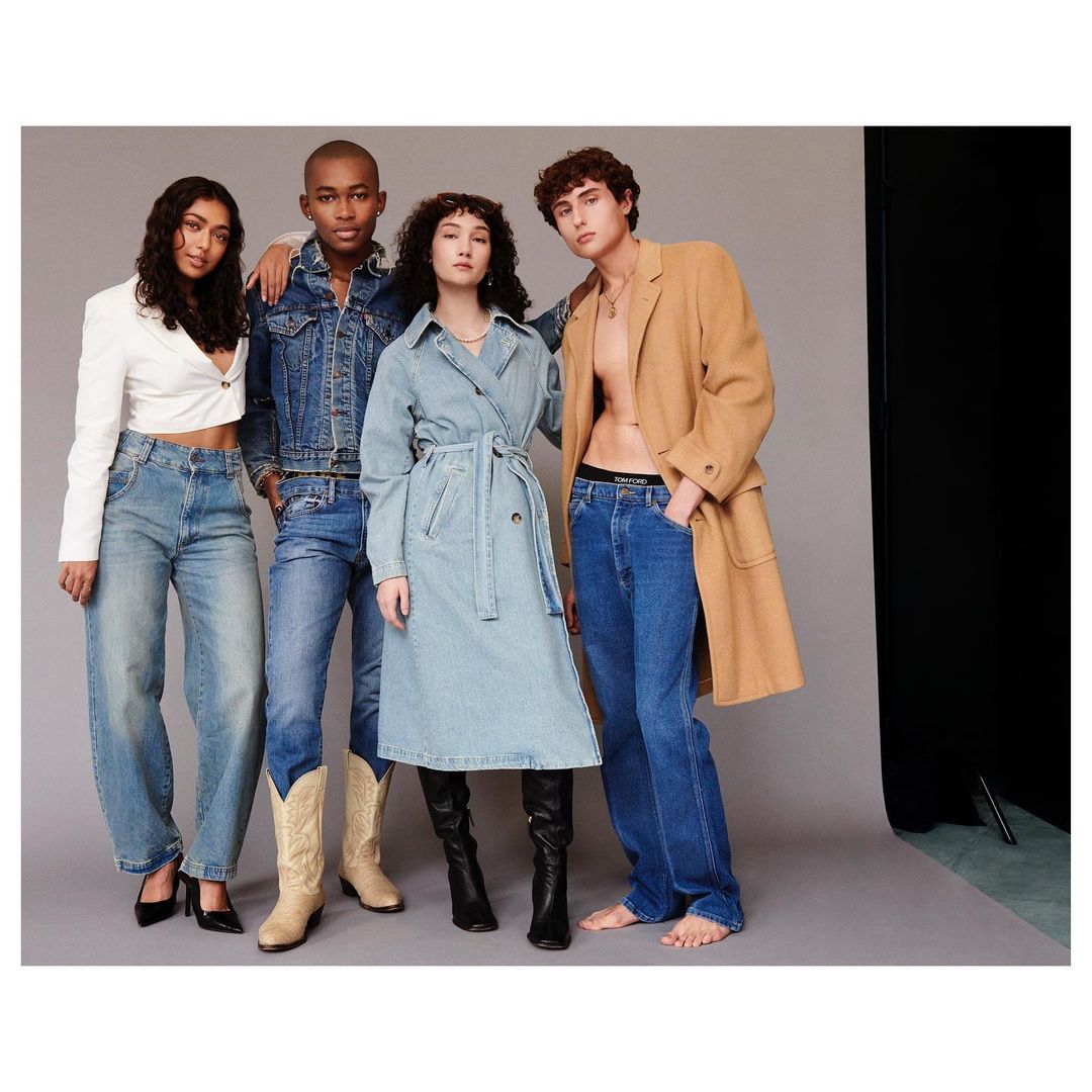 Four diverse adults showcase denim and neutral-toned outwear in a studio setting with gray backdrop for a fashion editorial shoot.