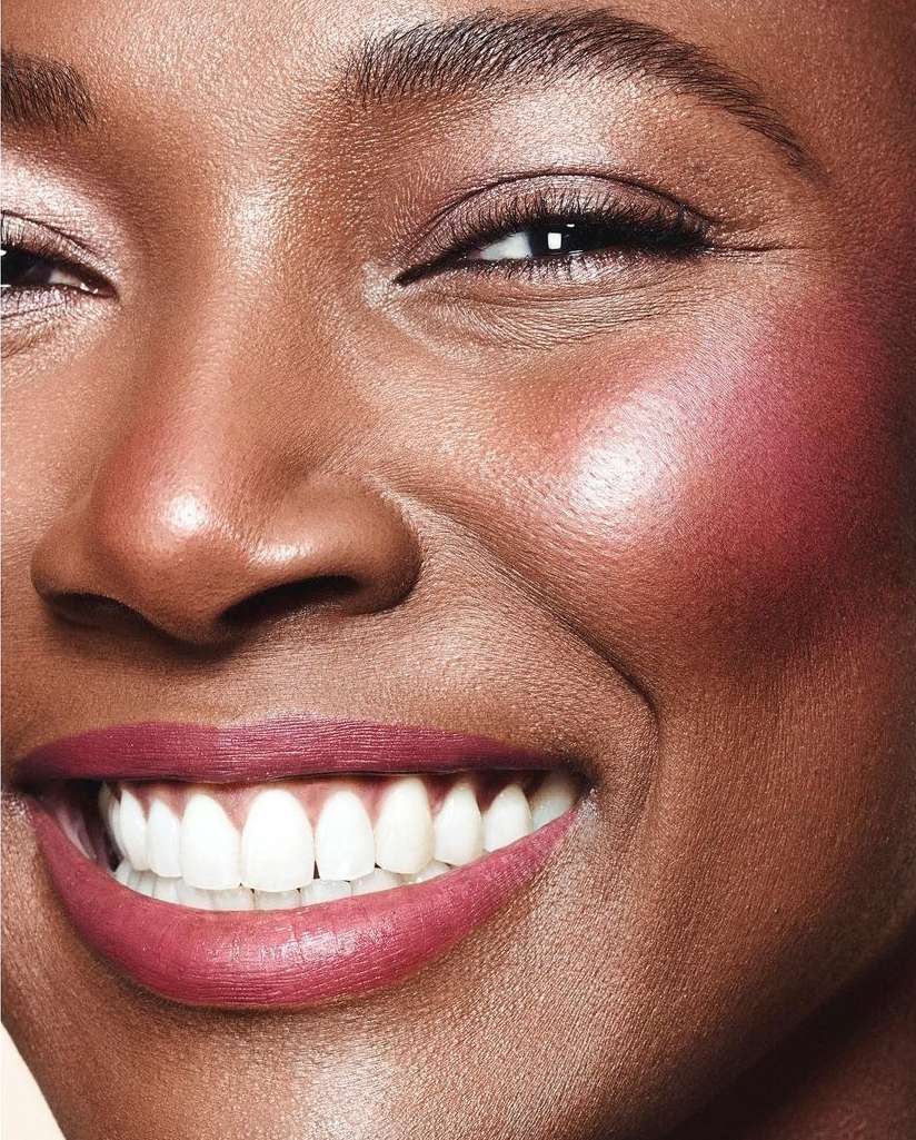 Close-up portrait of a smiling African-American woman showcasing flawless makeup, including blush, lipstick, and highlighted skin.