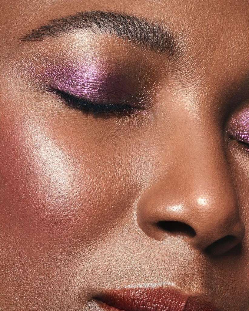 Close-up of a woman's face with closed eyes and purple eyeshadow. Beauty shot highlighting skin texture, eyebrow, and lip details.