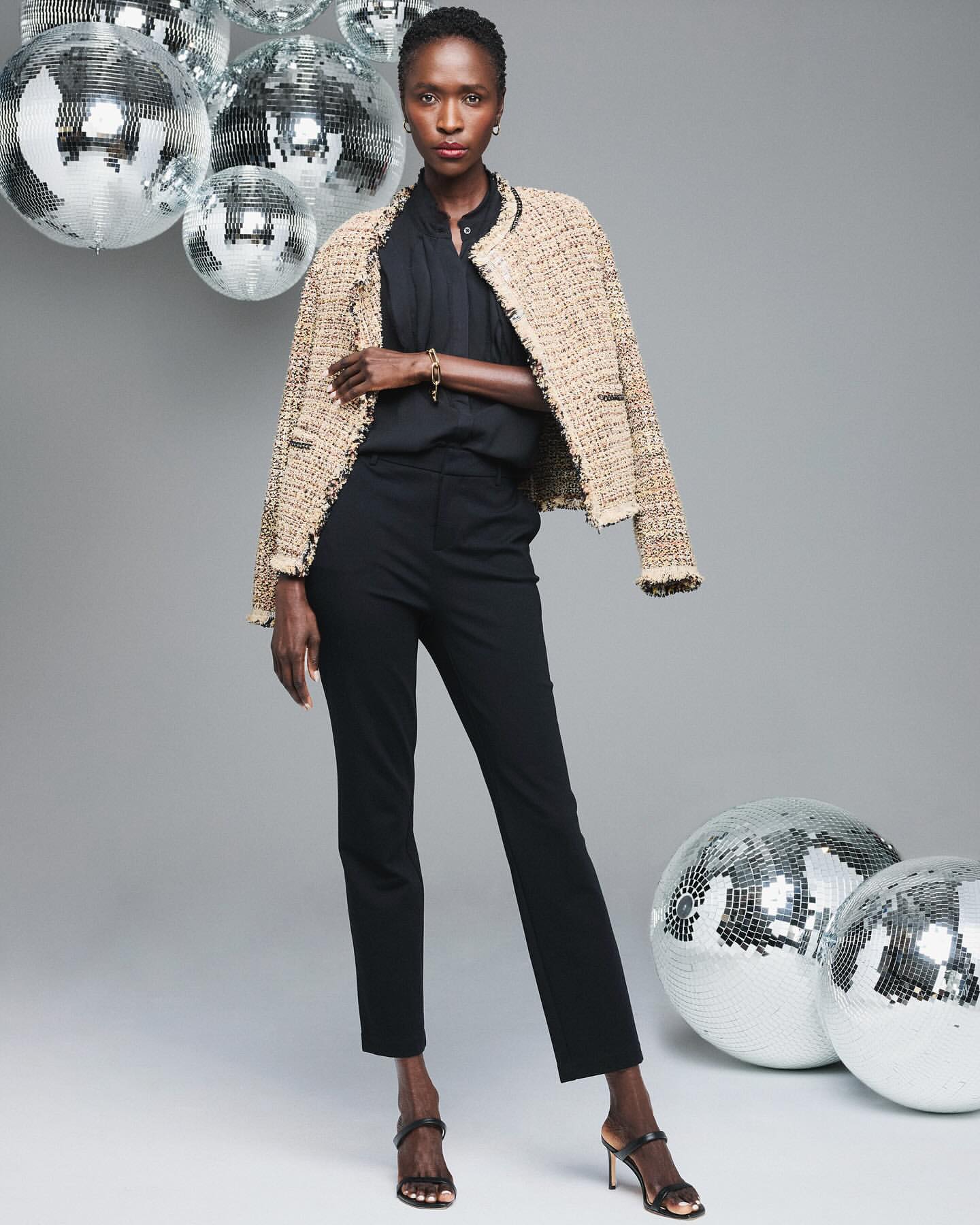 Elegant Black woman in a tweed jacket, black top, and trousers, posing in front of disco balls in a studio. Fashion editorial shot.