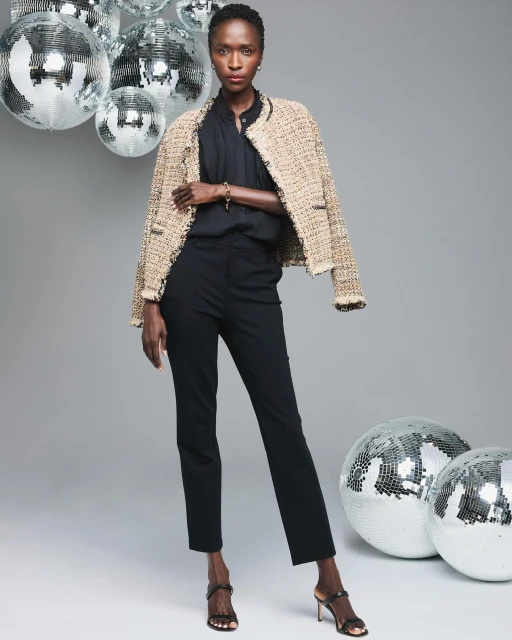 Elegant Black woman in a tweed jacket, black top, and trousers, posing in front of disco balls in a studio. Fashion editorial shot.