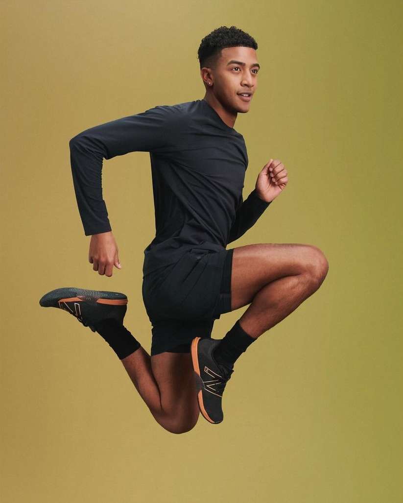 Athletic man in black activewear leaps against a graduated yellow background, showcasing dynamic movement and fitness.