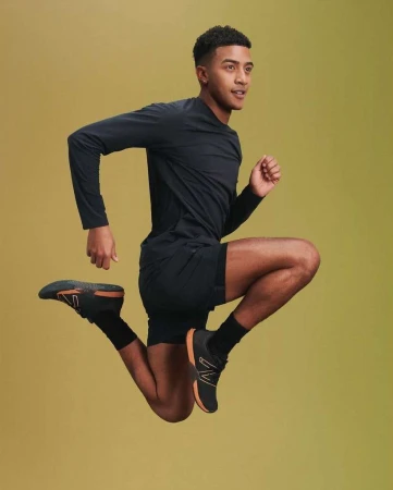 Athletic man in black activewear leaps against a graduated yellow background, showcasing dynamic movement and fitness.
