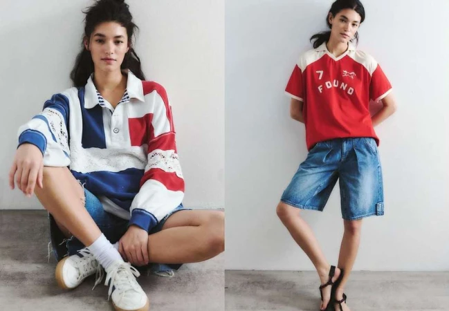 Two women pose against a white wall in colorful short denim outfits. One is sitting wearing a patchwork shirt and sneakers; the other stands in sandals.