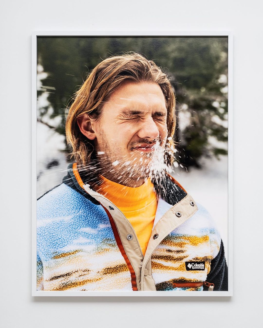 Framed studio portrait of a fair-skinned adult male in outdoors clothing with his eyes closed as water is splashed at his face.