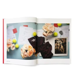 An open magazine page displays styled still-life photography with tennis balls, peach roses, documents, and clothing.