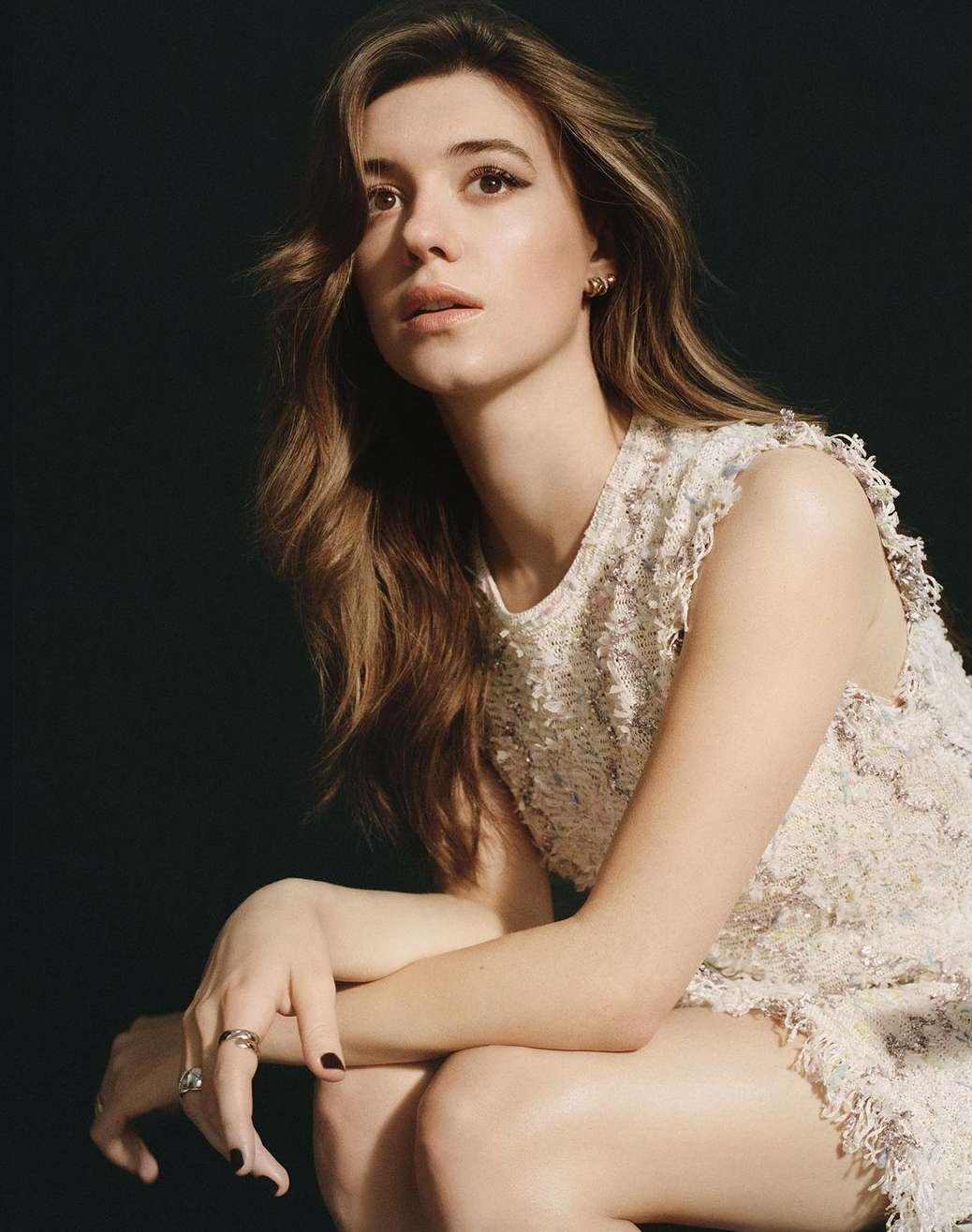 Portrait of a woman wearing a white textured dress and rings against a dark background, photographed by Buzz White in London.