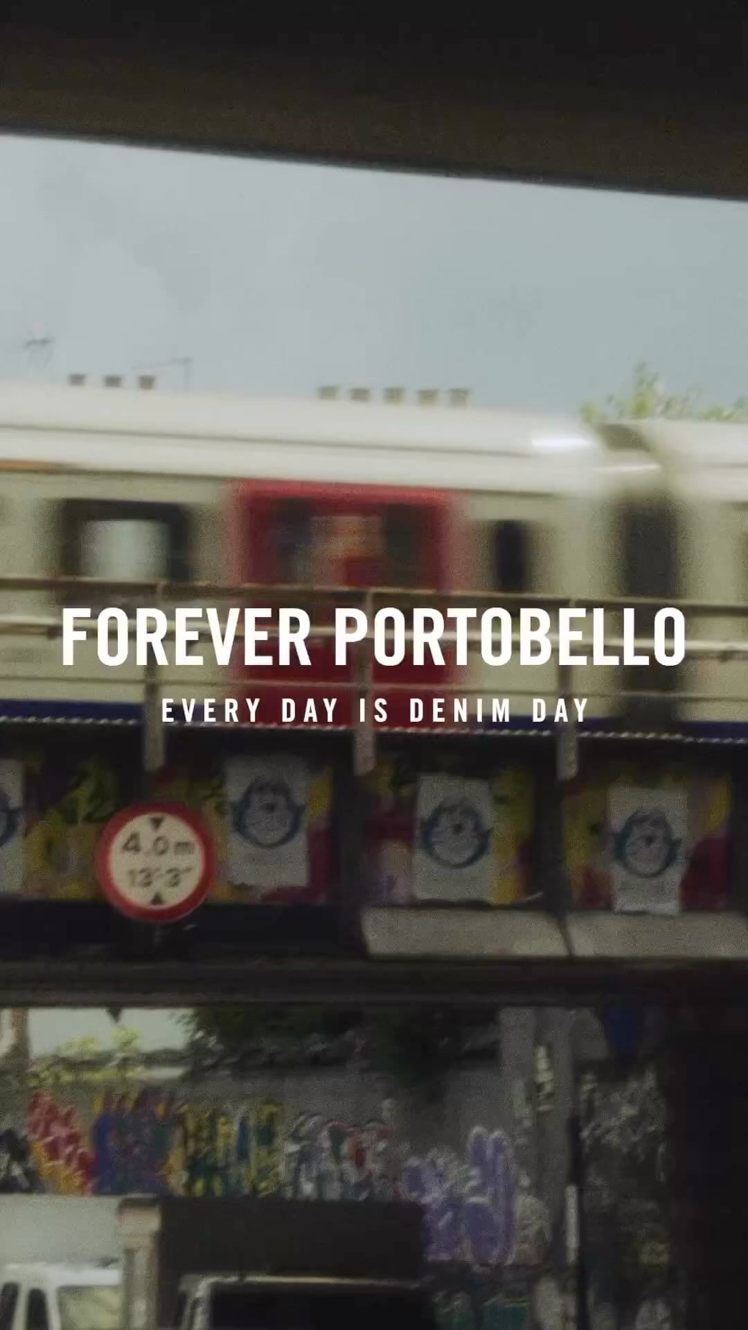 Motion blur of a speeding train passing a building with advertising and graffiti, filmed in a portrait aspect ratio.