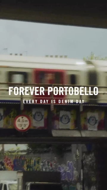 Motion blur of a speeding train passing a building with advertising and graffiti, filmed in a portrait aspect ratio.