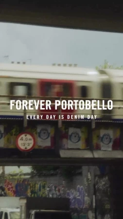 Motion blur of a speeding train passing a building with advertising and graffiti, filmed in a portrait aspect ratio.