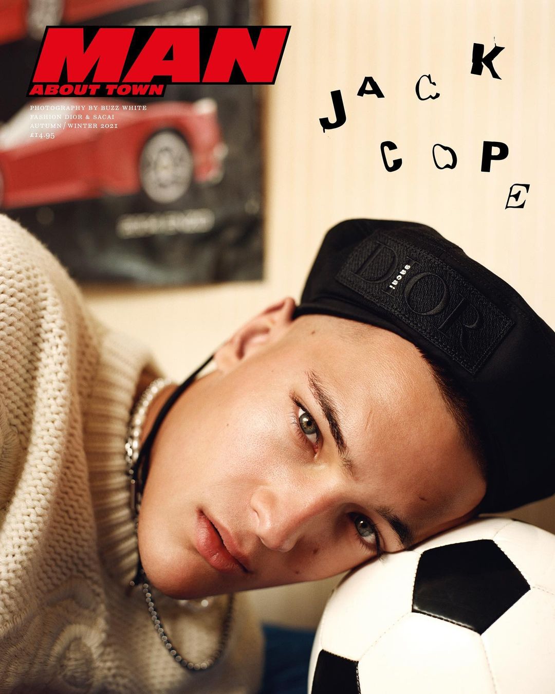 Close-up studio shot of a young adult with short hair, wearing a black beret and a sweater, resting his head on a soccer ball.