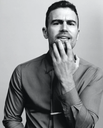 Portrait of a handsome adult male with his hand near his face, wearing a collared shirt and tie clip, against a plain background.