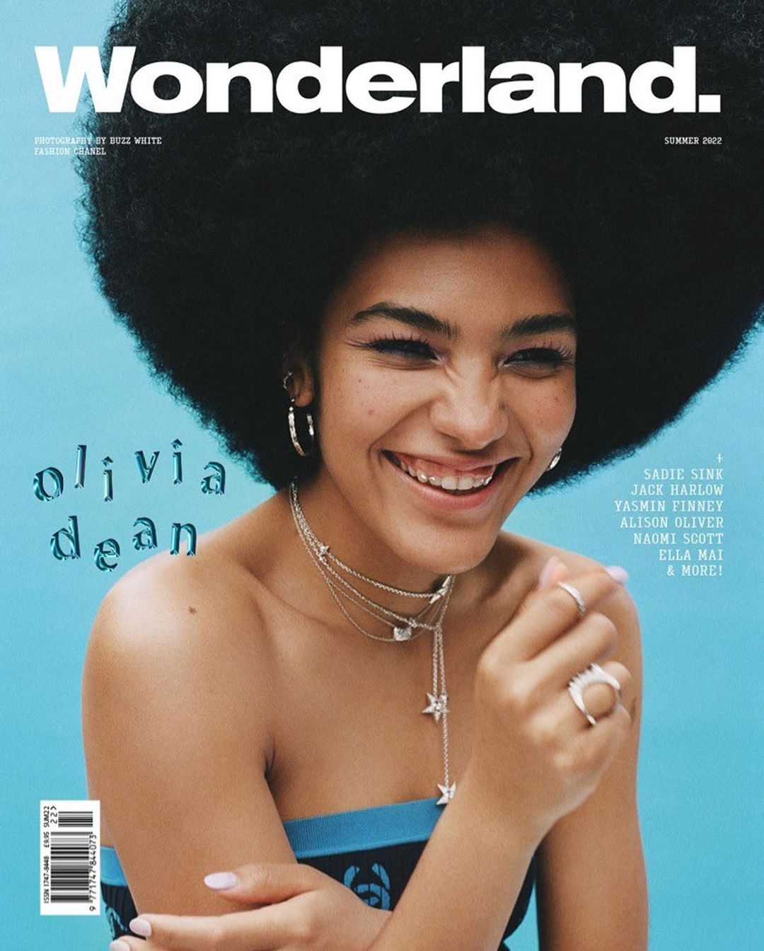 Wonderland Magazine cover featuring Olivia Dean, showcasing her afro hairstyle, stylish jewelry, and a bright, smiling face on a teal background.